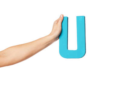 Female hand holding up the uppercase capital letter U isolated against a white background conceptual of the alphabet, writing, literature and typefaceの写真素材