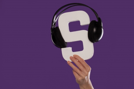 Female hand holding up the letter S with a set of headphones draped over the top over a purple studio backgroundの写真素材