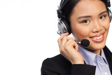 Smiling Asian woman wearing a headset and stylish business jacket, conceptual of a call centre, help...