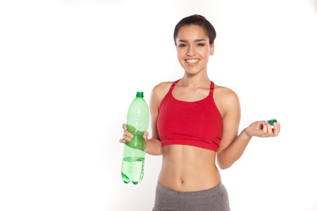Smiling shapely young woman wearing a sports bra standing looking at the camera with a large bottle of bottled water in her hand isolated on whiteの写真素材