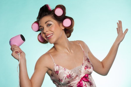 Fun portrait of an attractive woman in outsized pink haircurlers with a hairdryer in her hand posing for the camera against a blue backgroundの写真素材