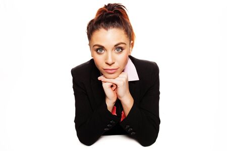 Beautiful pensive businesswoman sitting at her desk with her chin resting on her hands looking into the camera isolated on whiteの写真素材