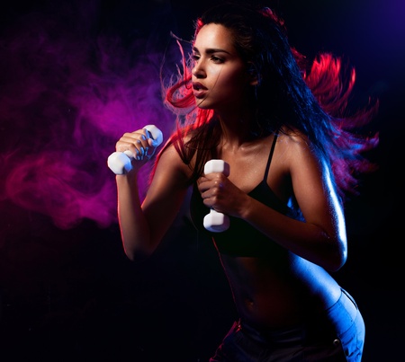 Determined fit sexy woman working out with dumbells on blue and violet smoky wave backgroundの写真素材