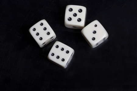 Macro photo of four white dices over a black background and a mirror surface