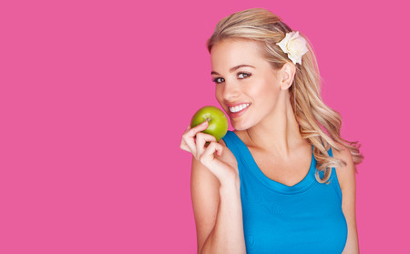 Beautiful healthy young woman with a fresh juicy green apple in her hand smiling and looking at the camera over a pink backgroundの写真素材
