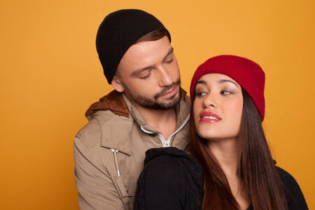 Beautiful young couple in love standing looking into each others eyes with a look of desire and longing, over an orange studio backgroundの写真素材