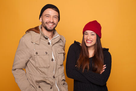 Trendy young couple wearing winter clothing such as long coats and beanie hats in a yellow backgroundの写真素材