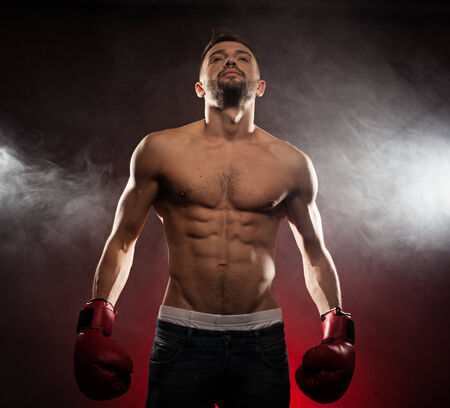 Low angle view of a shirtless fit caucasian boxer showing the abs and wearing red boxing glovesの写真素材