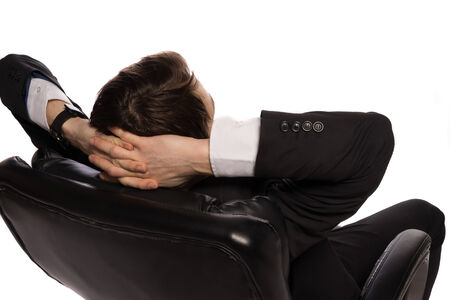 Rear view of a young Caucasian relaxed businessman sitting in a comfortable leather office chair, with the hands clasped behind his head, on white backgroundの写真素材
