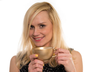Beautiful young blond woman with a lovely smile drinking from a golden cup she is holding in her hand, isolated on white with copyspaceの写真素材
