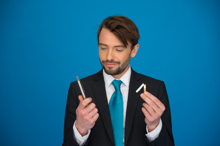 handsome businessman with e-cigarette wearing suit and tie on blue backgroundの写真素材