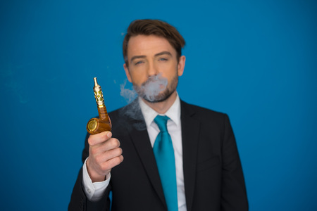 handsome businessman with e-cigarette wearing suit and tie on blue backgroundの写真素材
