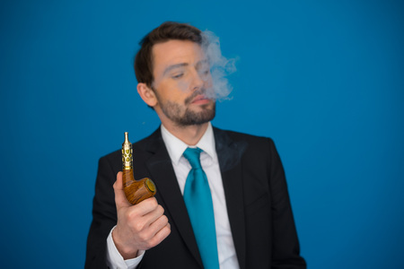 handsome businessman with e-cigarette wearing suit and tie on blue backgroundの写真素材