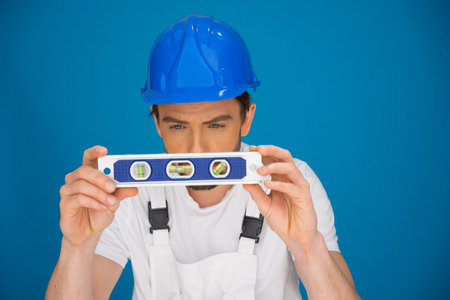 Workman viewing a spirit level concentrating as he bends forwards trying to read the position of the...