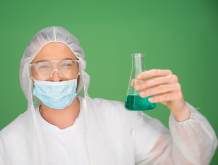 Male laboratory technician wearing a mask holding a chemical solution in a conical flask as he conducts experiments in the laboratoryの写真素材