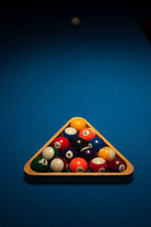 Racked set of numbered object pool balls in a triangular wooden rack ready for an eight-ball frame or game on a blue beize table with copyspaceの写真素材