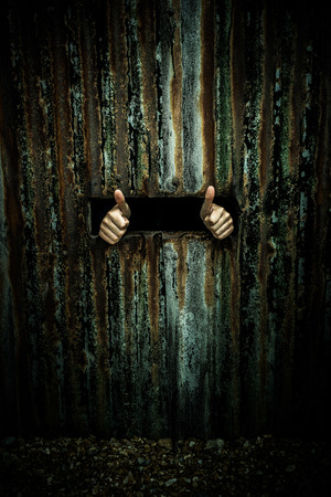 Hands showing thumbs up through a small narrow window of an old rusty wall, concept of positive thinking and humanityの写真素材