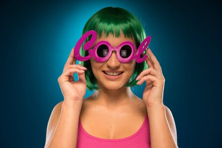 Smiling Pretty Young Lady with Green Short Hair, Wearing Pink Cool Shades. Isolated Blue Backgroundの写真素材