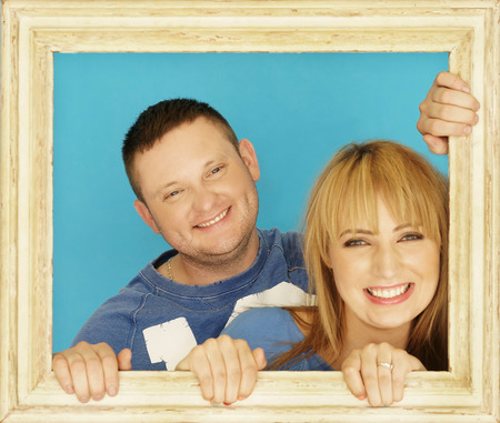 Loving couple in picture frame. Beautiful young couple looking through a picture frame and smilingの写真素材