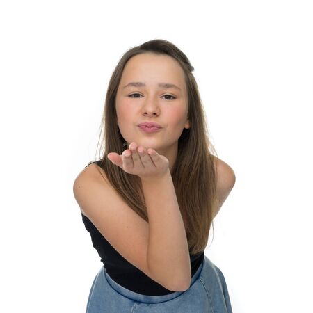 Playful pretty young girl blowing a romantic kiss at her boyfriend or sweetheart as she flirts seductively with him, isolated on whiteの写真素材