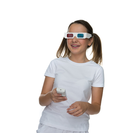 Young girl with her hair in pigtails wearing 3d stereoscopic glasses and holding a remote control for a video or film, ioslated on whiteの写真素材