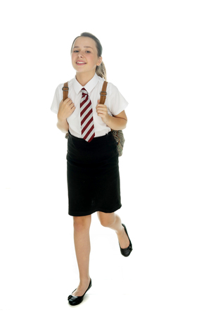 Happy attractive young girl in school uniform with a backpack over her shoulders running along with a cheerful smile, on whiteの写真素材