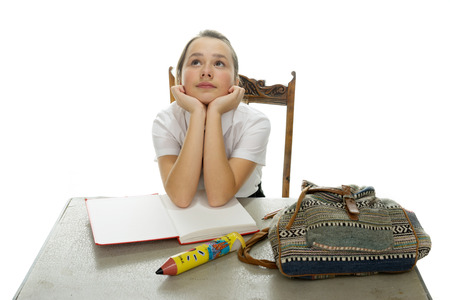 Young schoolgirl hoping for an answer sitting at her desk with her textbooks and backpack staring hopefully up into the air, on whiteの写真素材
