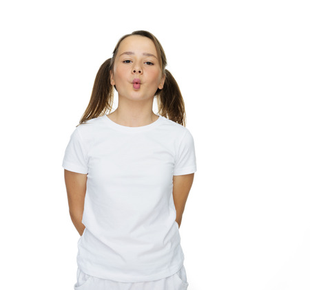 Cute young girl puckering up for a kiss standing with her hands behind her back leaning forwards with pouting lips, isolated on whiteの写真素材