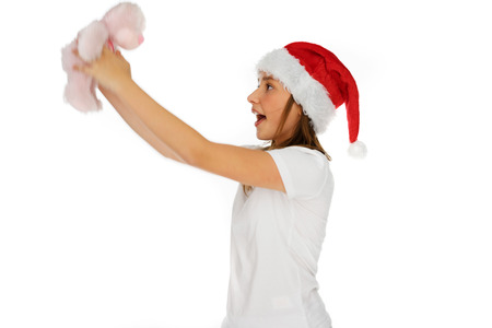 Excited young girl in a Santa Hat holding up a pink toy teddy bear that she has just received as a Christmas gift, on whiteの写真素材