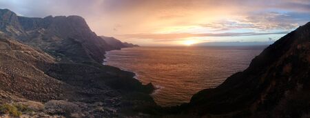 Colorful panoramic sunset or sunrise over a tranquil ocean and coastline on a cloudy day viewed from...