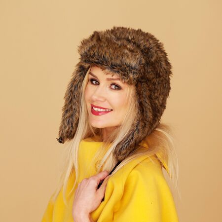 Pretty young woman in stylish winter fashion wearing an elegant bright yellow top and fur hat...