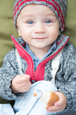 happy little baby boy wearing hat eating breadの写真素材
