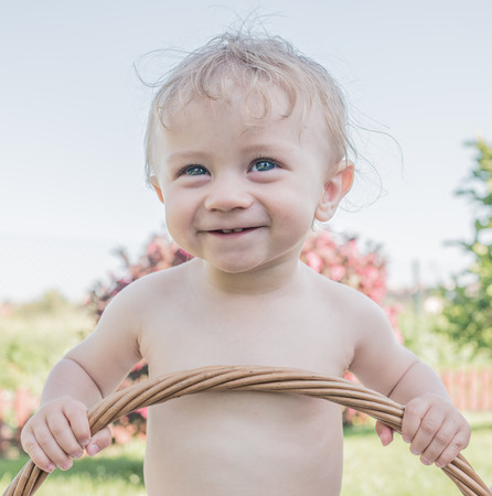Close up Adorable White Shirtless Baby at the Garden, Holding the Basket Handle While Smiling Into the Distance.の写真素材