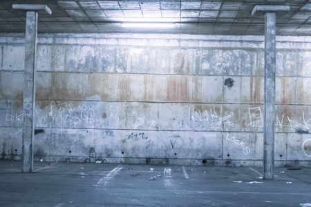 Empty commercial parking garage with a grunge concrete brick wall, overhead lighting and pillars with empty baysの写真素材