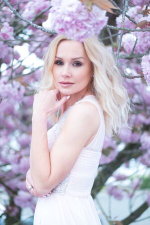 Gorgeous dreamy young woman with long blond hair standing in spring blossom looking up into the air with a faraway expression, close up view of her faceの写真素材
