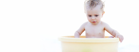 Cute White Baby Playing in a Yellow Bath Basin Alone, Isolated on White Background, Emphasizing Copy Space.の写真素材