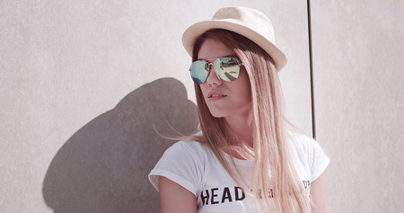 Close up Stylish Young Attractive Woman Wearing Hat and Sunglasses, Leaning Against the Wall and Looking Into Distance.の写真素材