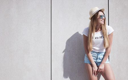 Happy Stylish Young Woman Leaning Against Plain Wall with Copy Space and Looking to the Right of the Frame.の写真素材