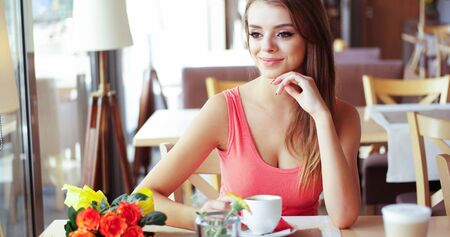 Portrait of Smiling Young Woman with Mug of Coffee Sitting in Sunny Window Seat of Trendy Cafe Restaurantの写真素材