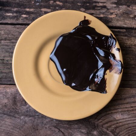 Melted dark chocolate on the yellow plate on the wooden tableの写真素材