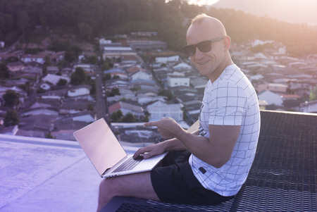 Outdoors portrait of handsome young man in sunglasses holding laptop computer on his knees and...