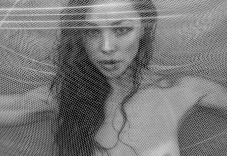 Black and white closeup portrait photo of sensual beautiful brunette woman trapped in the fishnet...