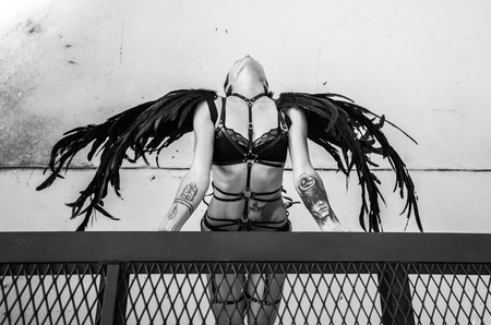 Top view black and white photo of beautiful seductive angel woman wearing lingerie and leather belts on the roof over white wallの写真素材
