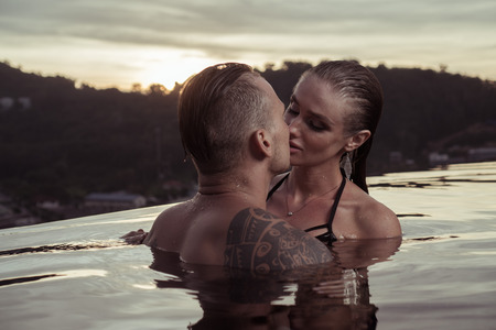 Romantic sensual couple alone in infinity swimming pool over beautiful tropical and sunset sky backgroundの写真素材
