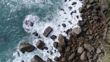 Aerial top view of sea waves hitting rocks on the beach in Phuket, Thailand
