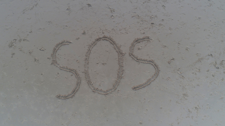 Top view photo of SOS written in sand on tropical beach. Concept photo of help emergency desperation lost and hopeの写真素材