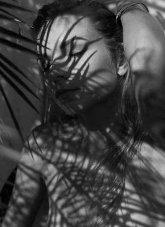 Black and white portrait photo of pretty blonde woman with palm tree leaves pattern shadow on her face and bodyの写真素材