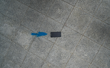 Top view of mobile phone isolated next to blue arrow painted on asphalt street, can be used as...