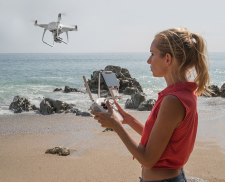 Pretty woman standing on the beach with remote controller of drone over sea and sky background