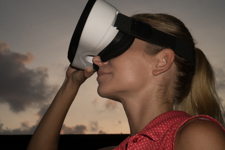 Closeup portrait of woman having fun with virtual reality glasses over beautiful summer sunset sky treeの写真素材